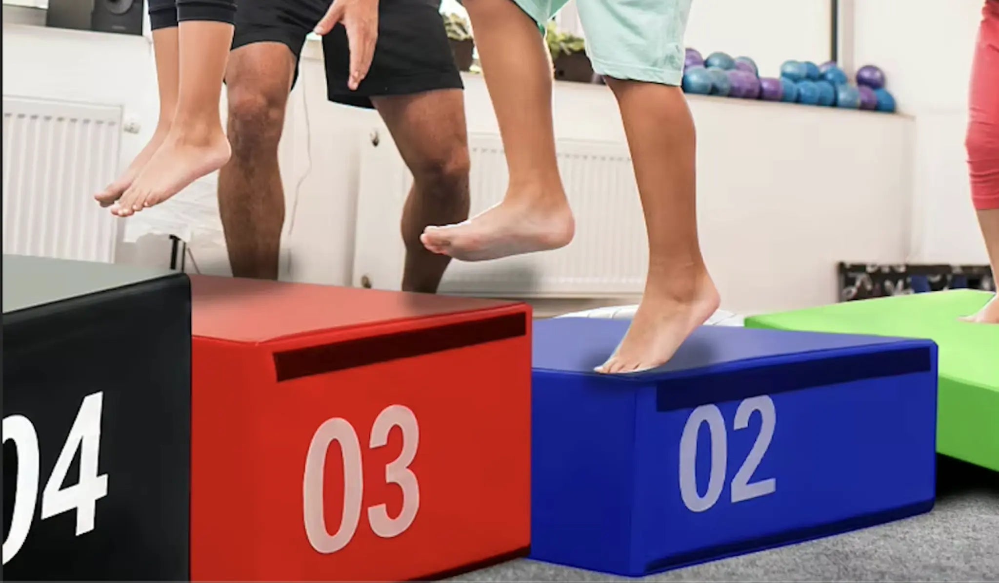 Close-up of bare feet of child and adult jumping onto soft foam plyo boxes (numbered 02, 03, 04), emphasizing safe, explosive family training.