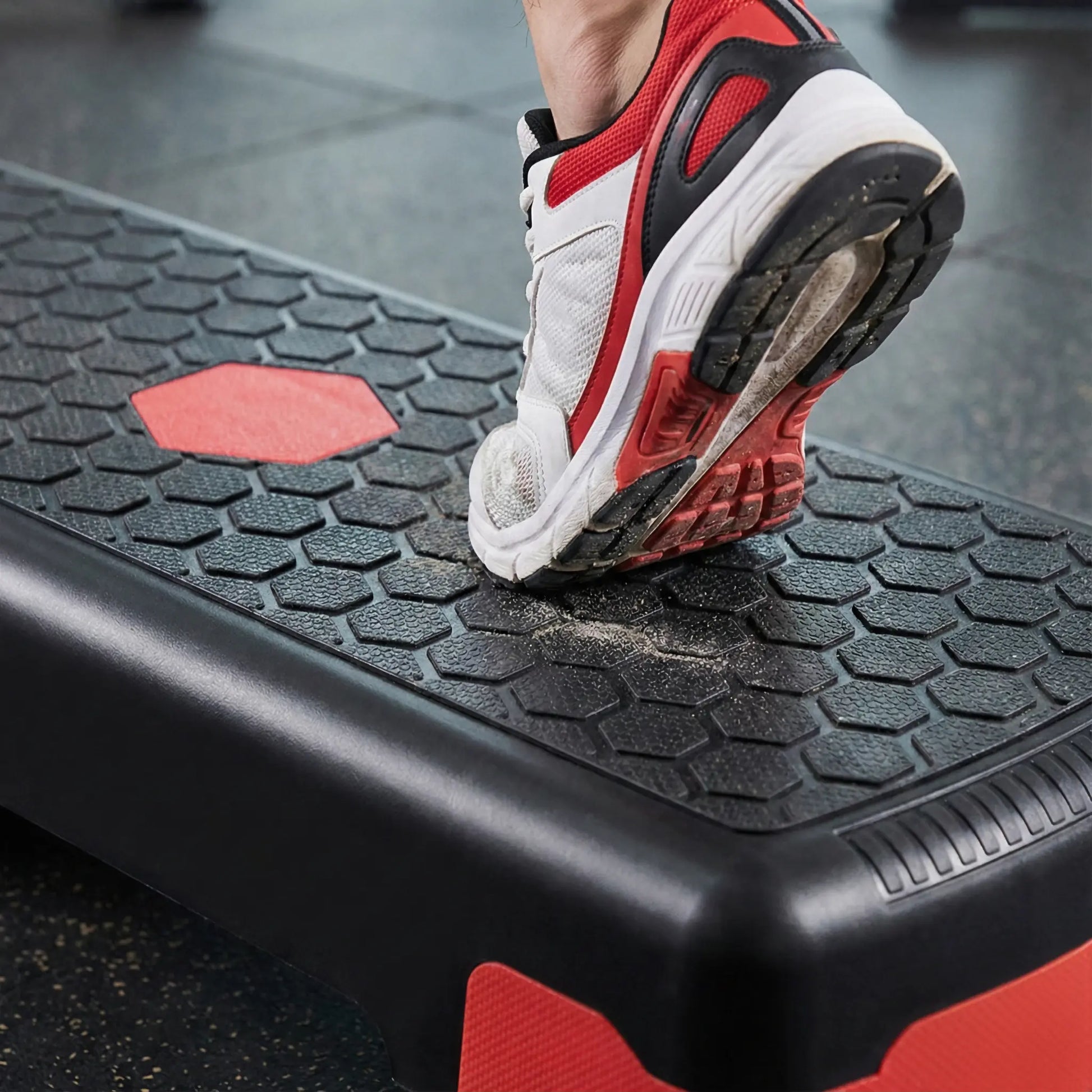 Person stepping onto a non-slip black and red aerobic step in a gym setting