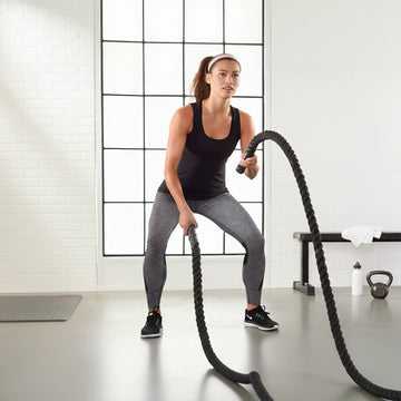Woman using a battle rope indoors on a wooden floor for functional training
