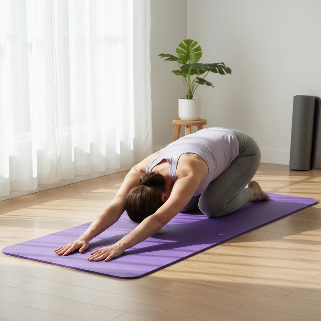 Person stretching in child’s pose on a purple exercise mat in a bright home studio.
