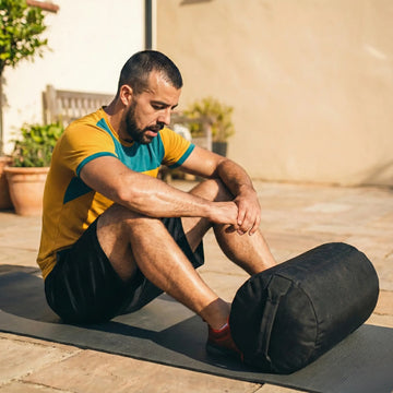 Man resting on a yoga mat after a sandbag workout on a sunny patio.