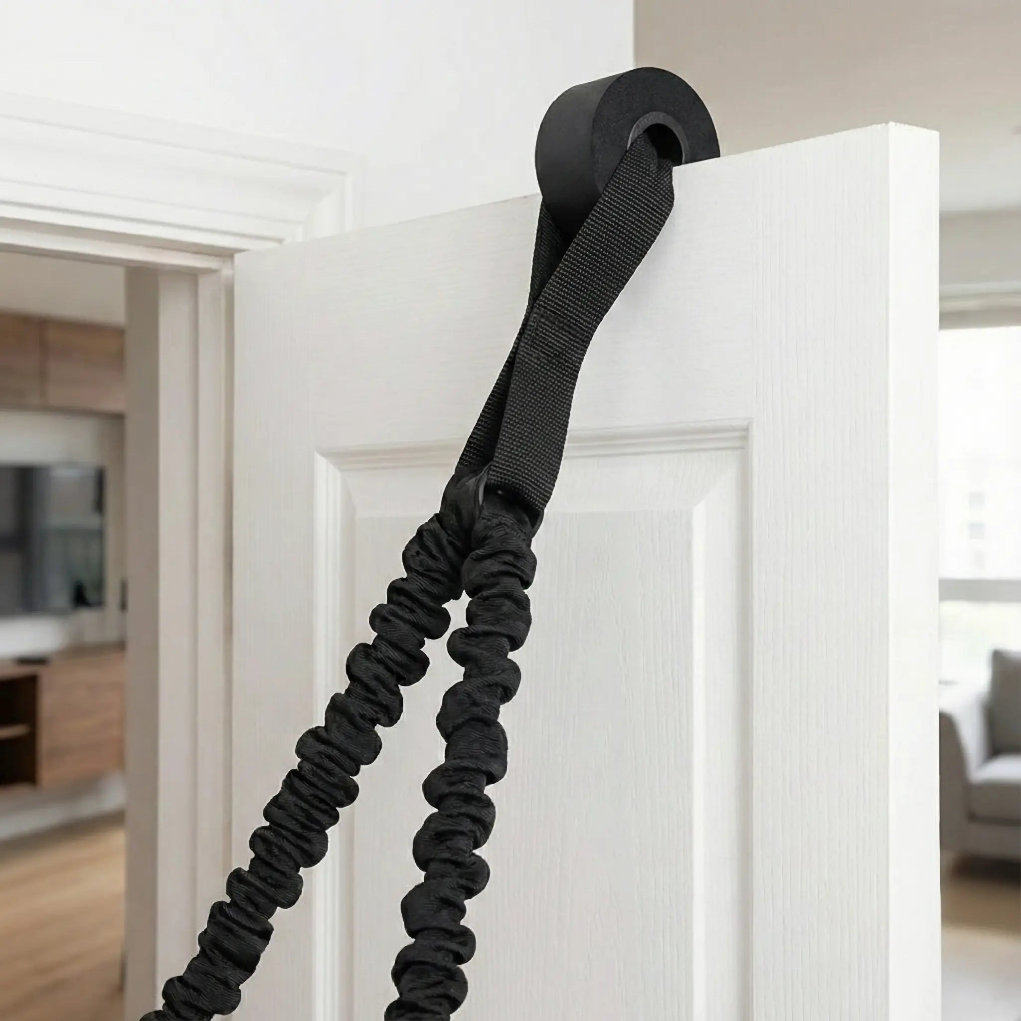 Close-up view of a resistance band door anchor strap securely fastened in a white door frame, with the heavy-duty black nylon band threaded through for home training.
