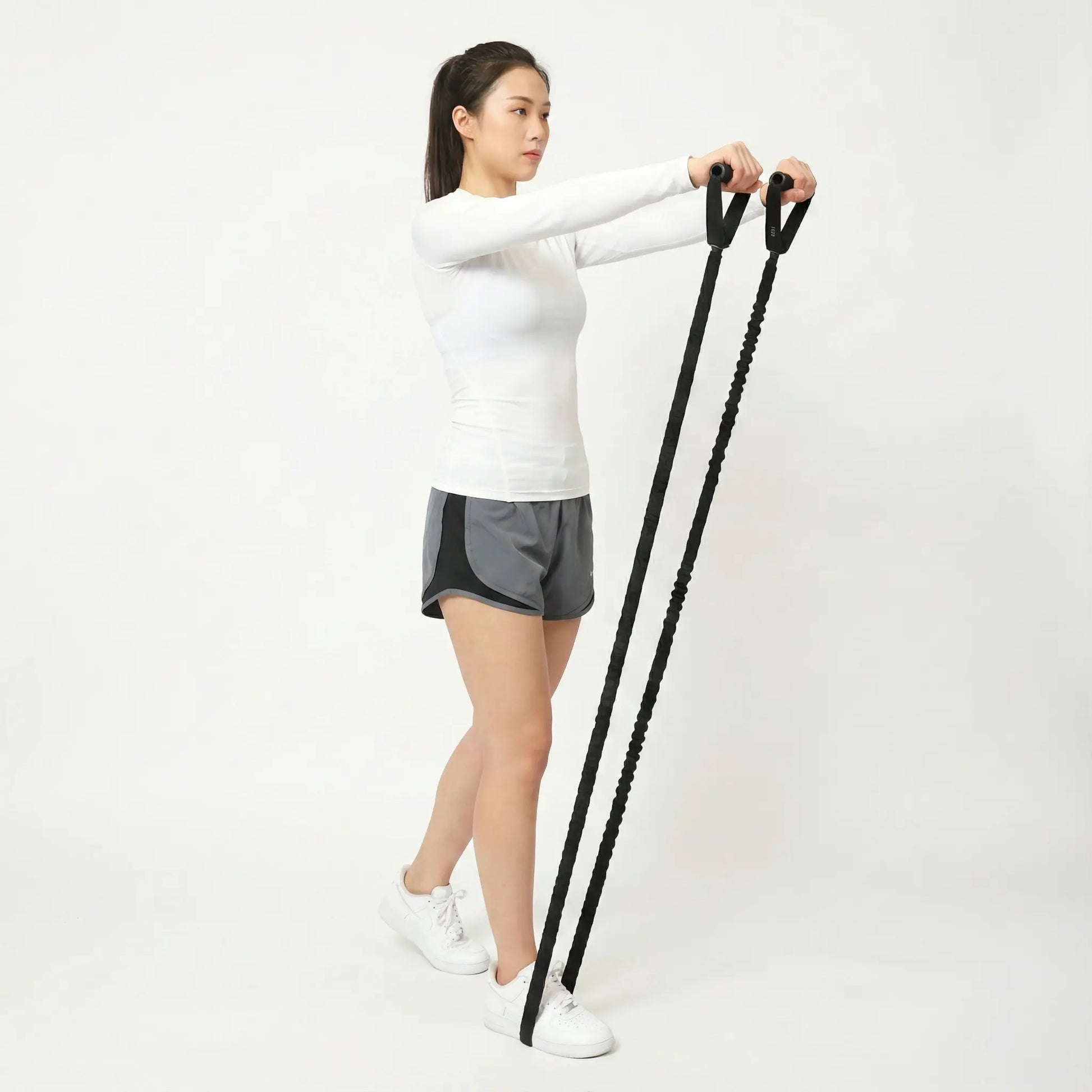 Fit woman performing a front raise exercise with heavy-duty black resistance bands against a white background.