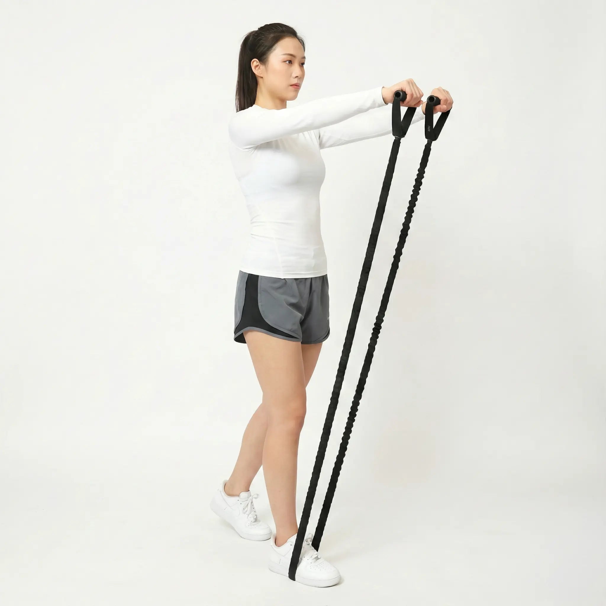Fit woman performing a front raise exercise with heavy-duty black resistance bands against a white background.