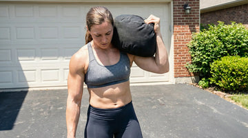 Woman lifting a sandbag outdoors in front of a garage.