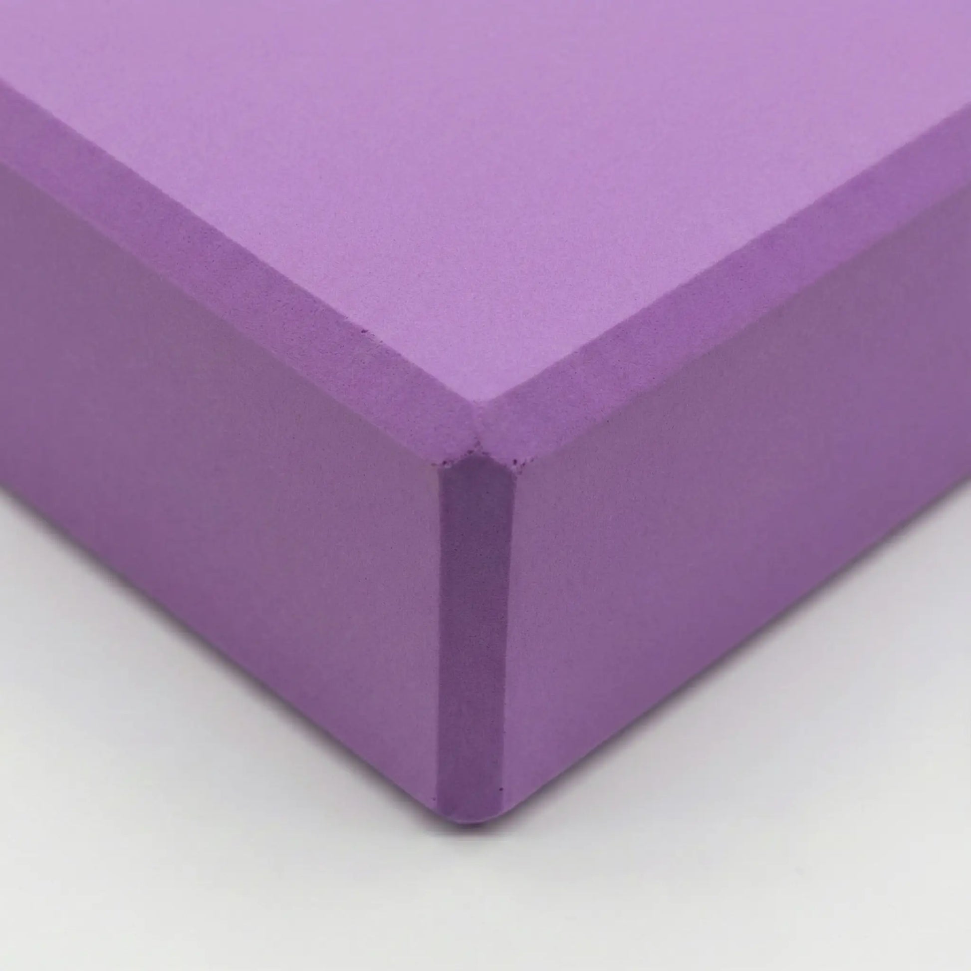 Close-up of a purple yoga block showing the bevelled corner and texture.