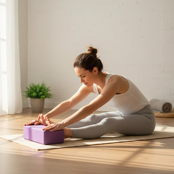 Woman using a purple yoga block to support a seated forward fold.